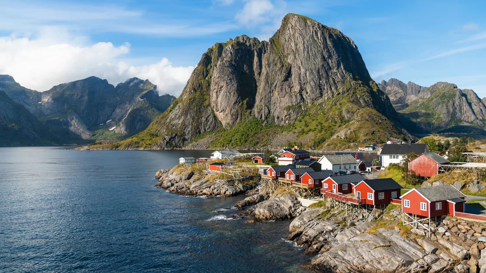 Rote Holzhäuser am Fjordufer vor einem schroffen Felsmassiv